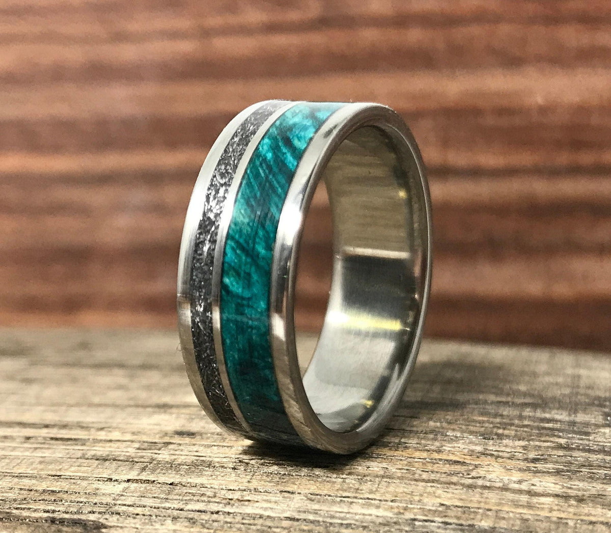 A silver-colored ring standing upright on a wooden surface, featuring a textured metallic inlay beside a vibrant green wood inlay.