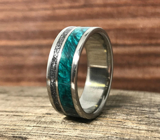 A silver-colored ring standing upright on a wooden surface, featuring a textured metallic inlay beside a vibrant green wood inlay.