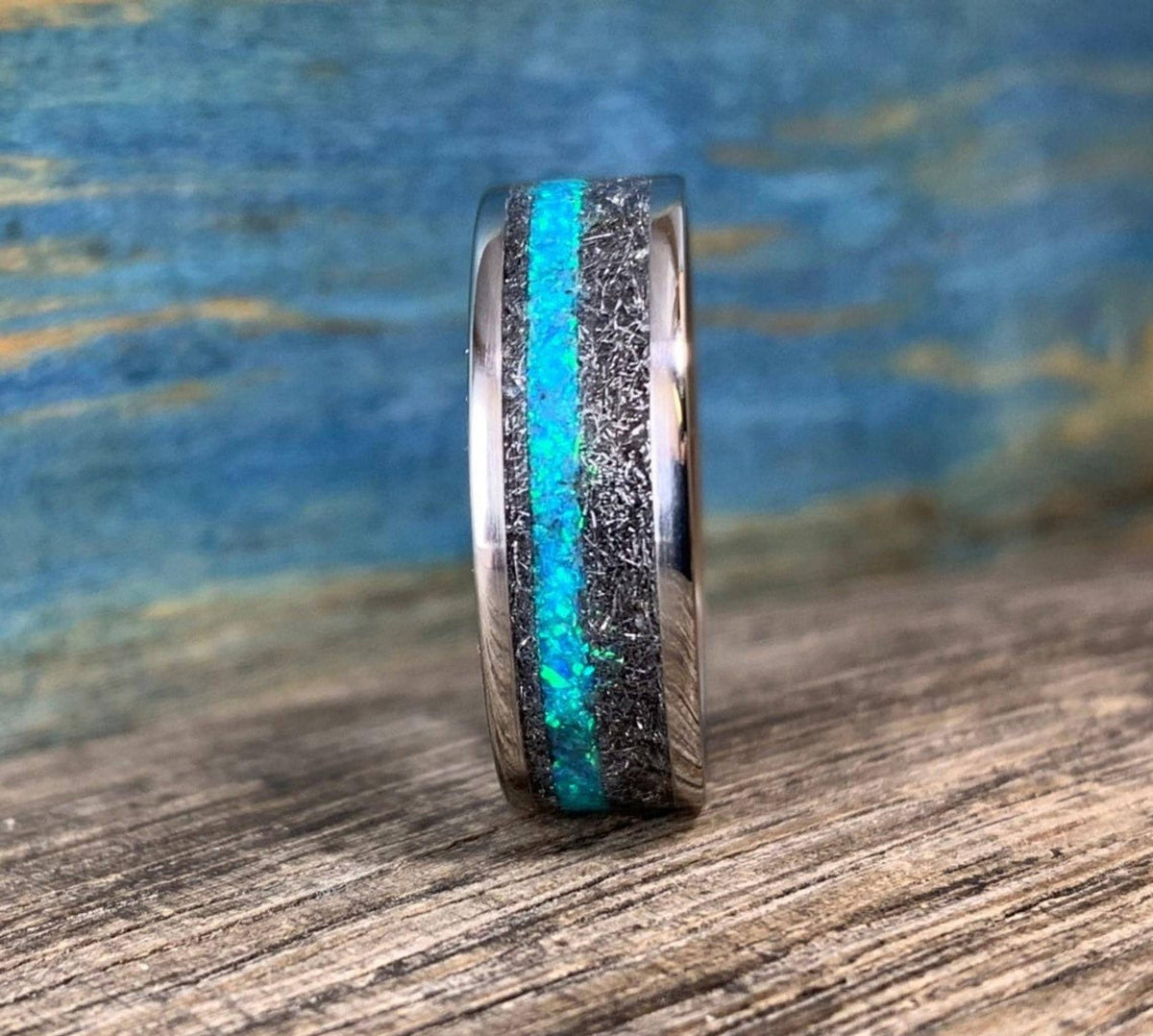 A straight-on view of the ring showcases its vibrant teal and blue opal stripe running through the textured meteorite band.