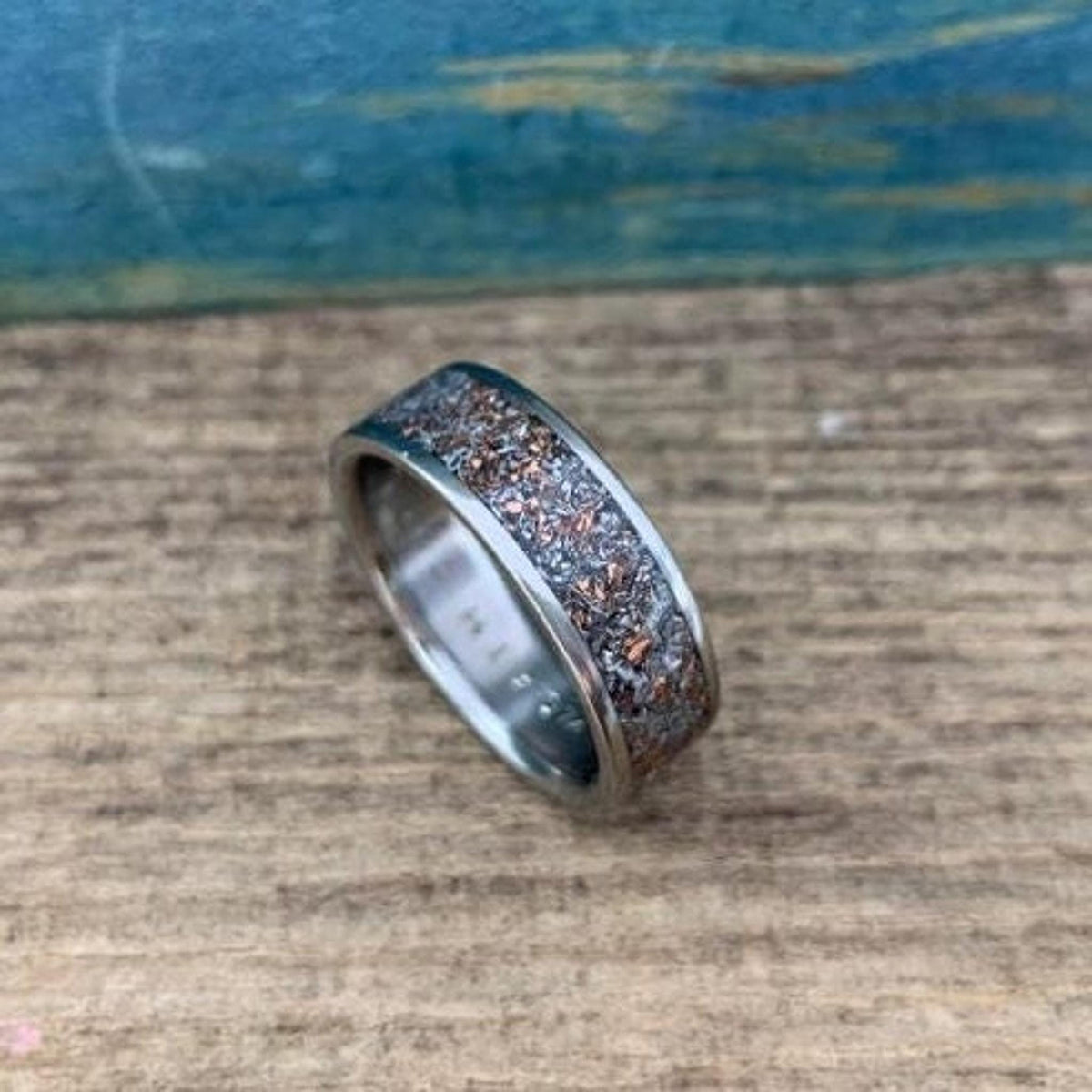 An angled view of a textured inlaid ring on a rustic wooden table.