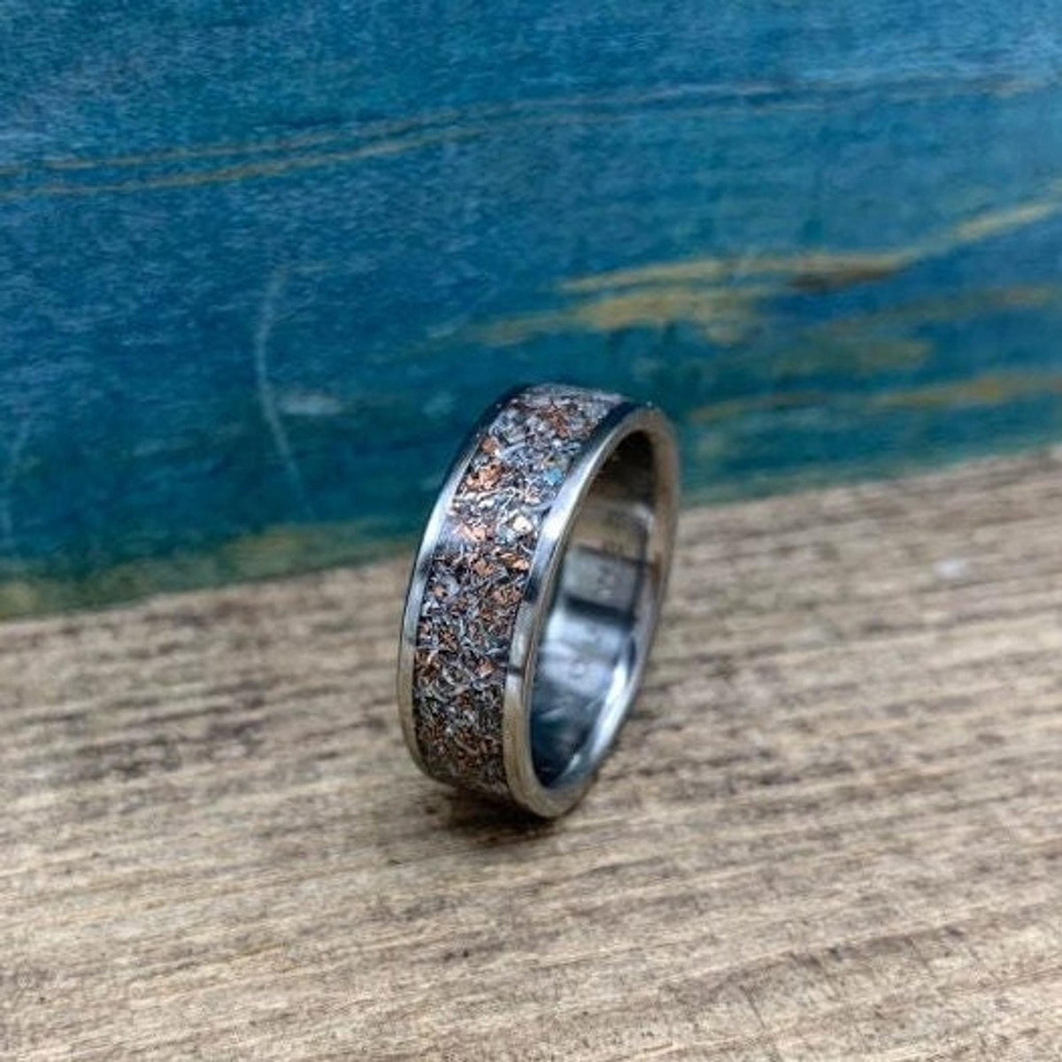 A side profile of the patterned inlaid band resting on a textured wooden surface.