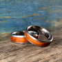 Two metal rings with wood inlay rest angled on a rustic wooden surface against a blue textured backdrop.