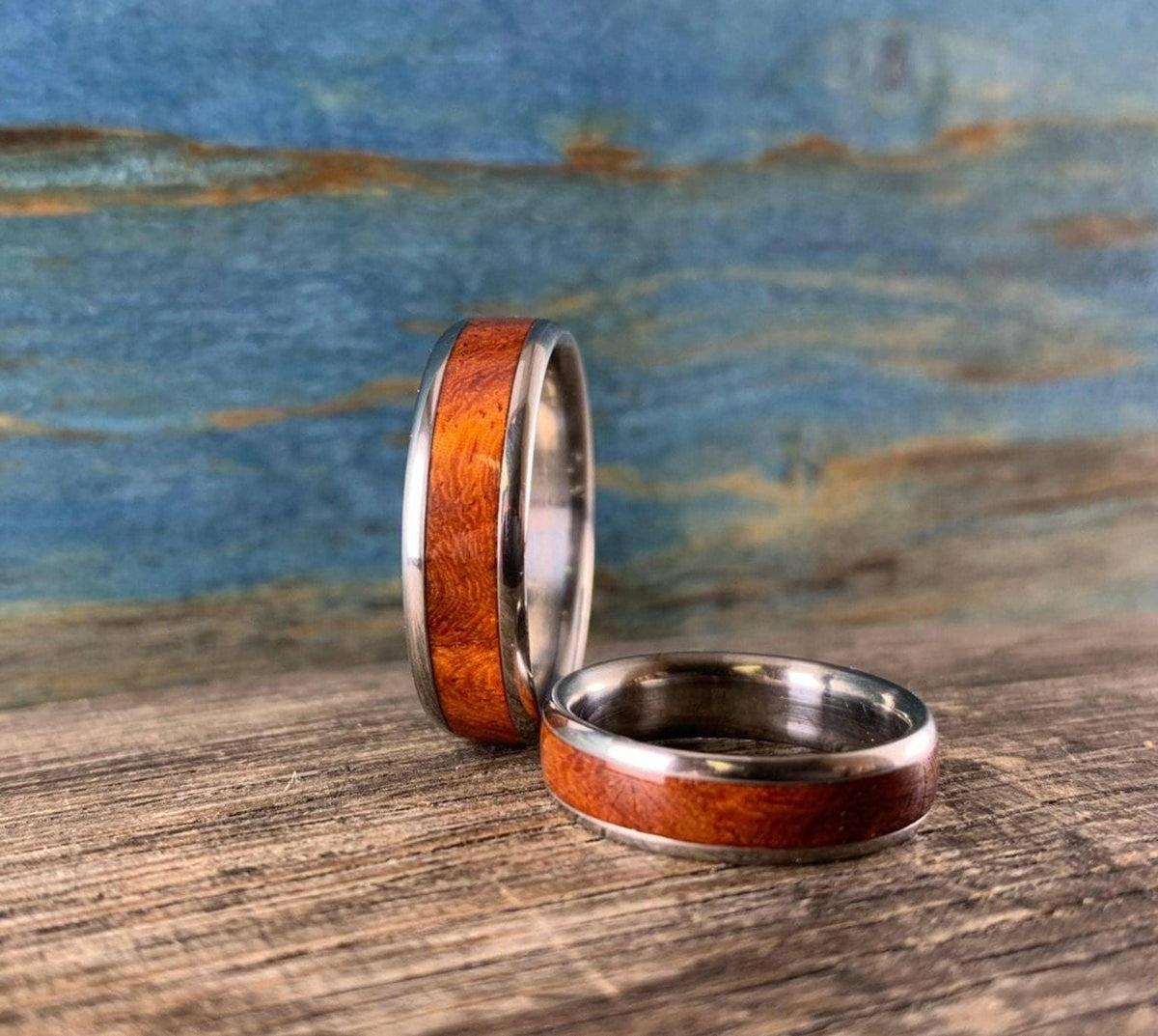 A single upright metal ring with a warm wood inlay stands beside another ring lying flat on wood.