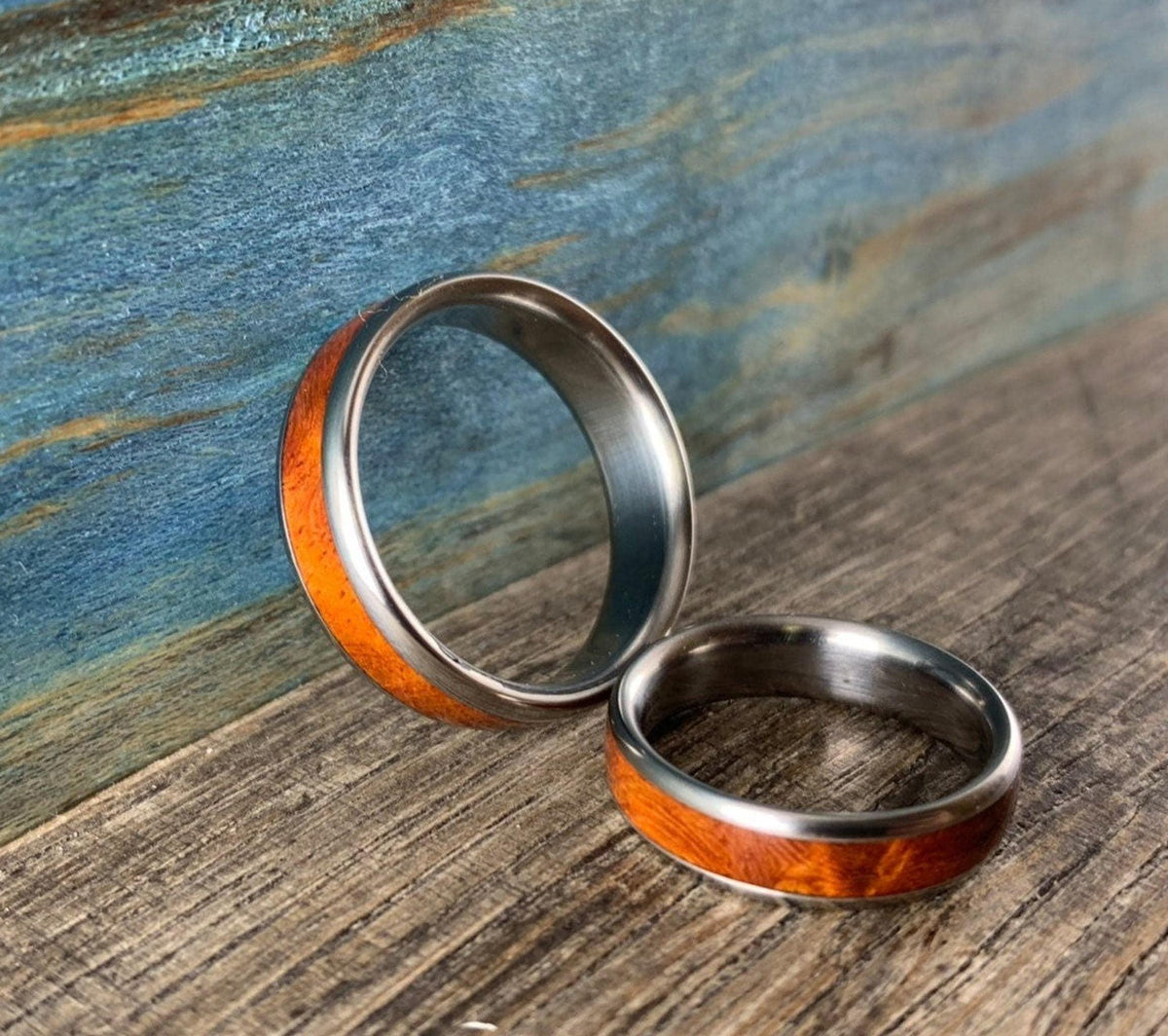 Two metal rings with wooden inlays rest at an angle on a weathered wooden surface.