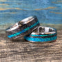 Two wedding bands made of titanium with meteorite inlays and bright blue-green opal stripes rest on a wooden surface.