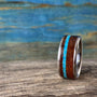 A ring with a wooden body and vibrant turquoise inlay stands vertically on a weathered wooden surface.