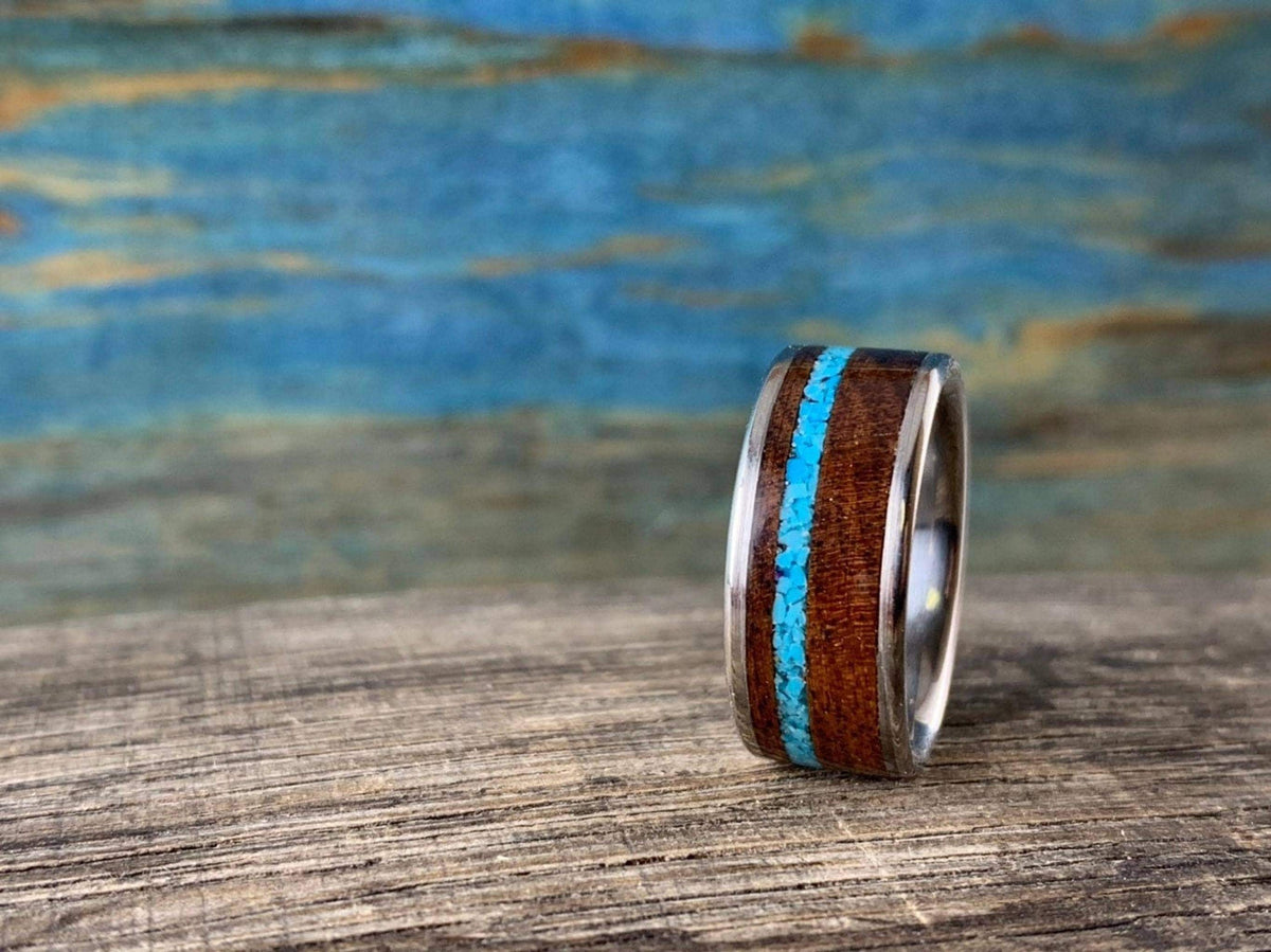 A ring with a wooden body and vibrant turquoise inlay stands vertically on a weathered wooden surface.