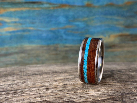 A ring with a wooden body and vibrant turquoise inlay stands vertically on a weathered wooden surface.