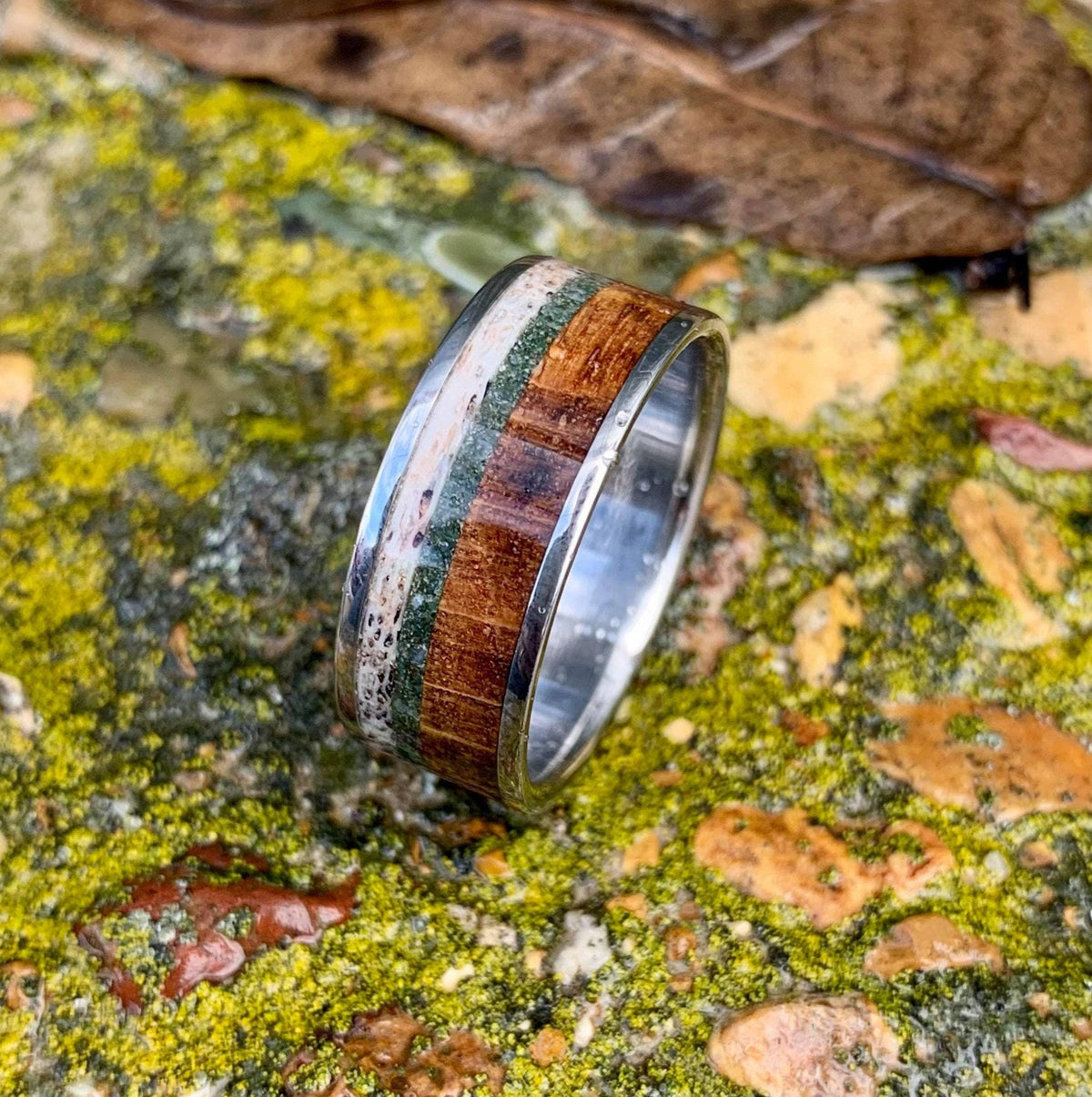 A close-up view of the multi-material ring showing the grain of the wood inlay next to green moss agate and antler.