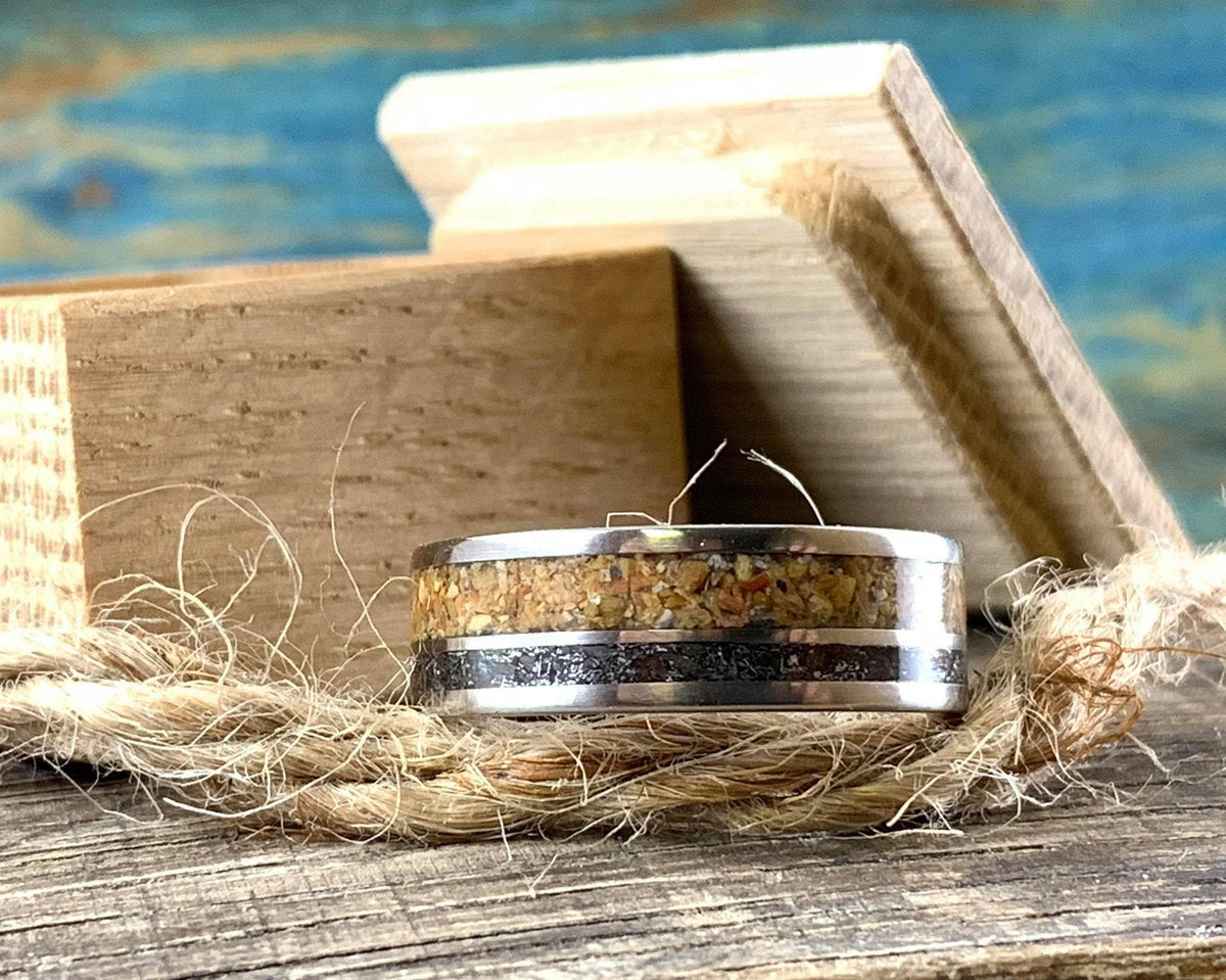 A wooden ring box and a metal ring inlaid with wood and dark meteorite sit on a wooden surface with twine.