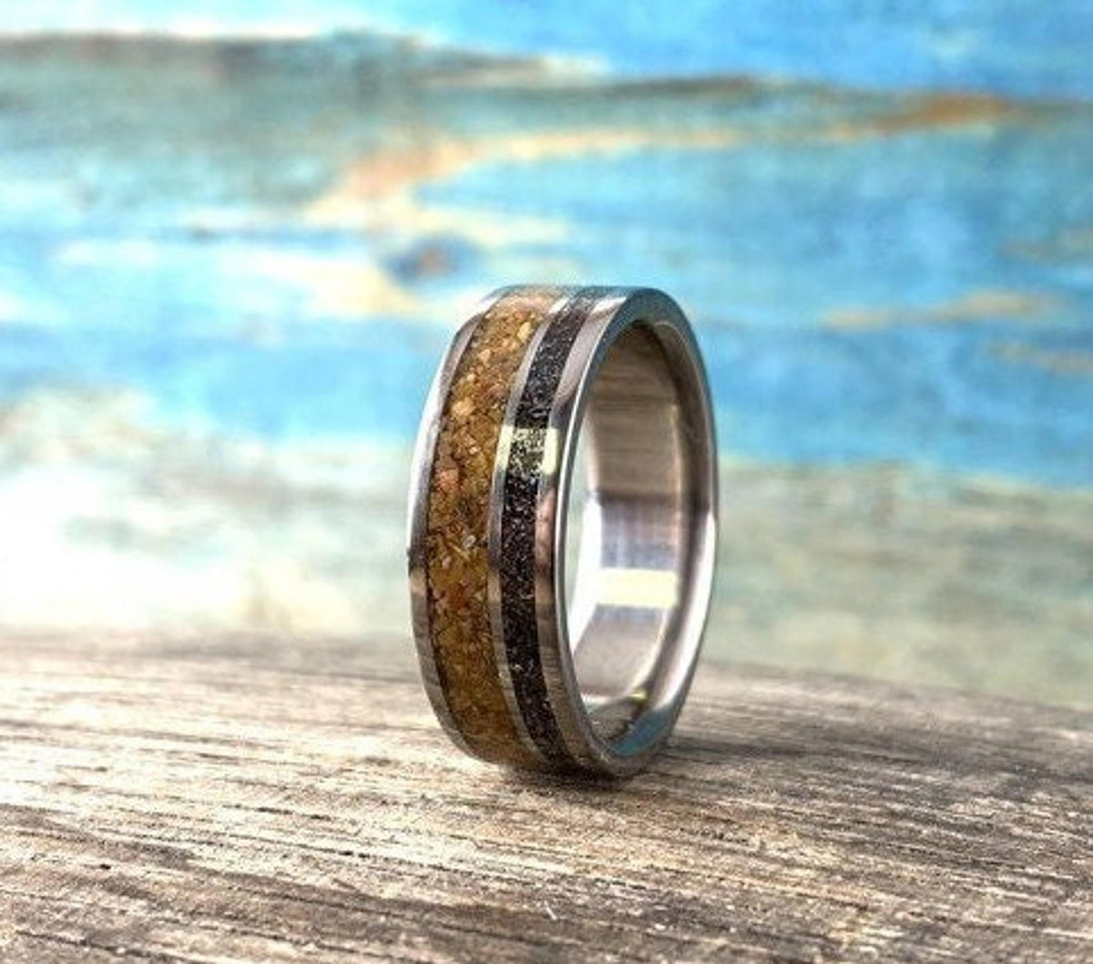 A close-up shot of a metal ring featuring a wide band of textured brown wood and a narrow dark meteorite inlay.