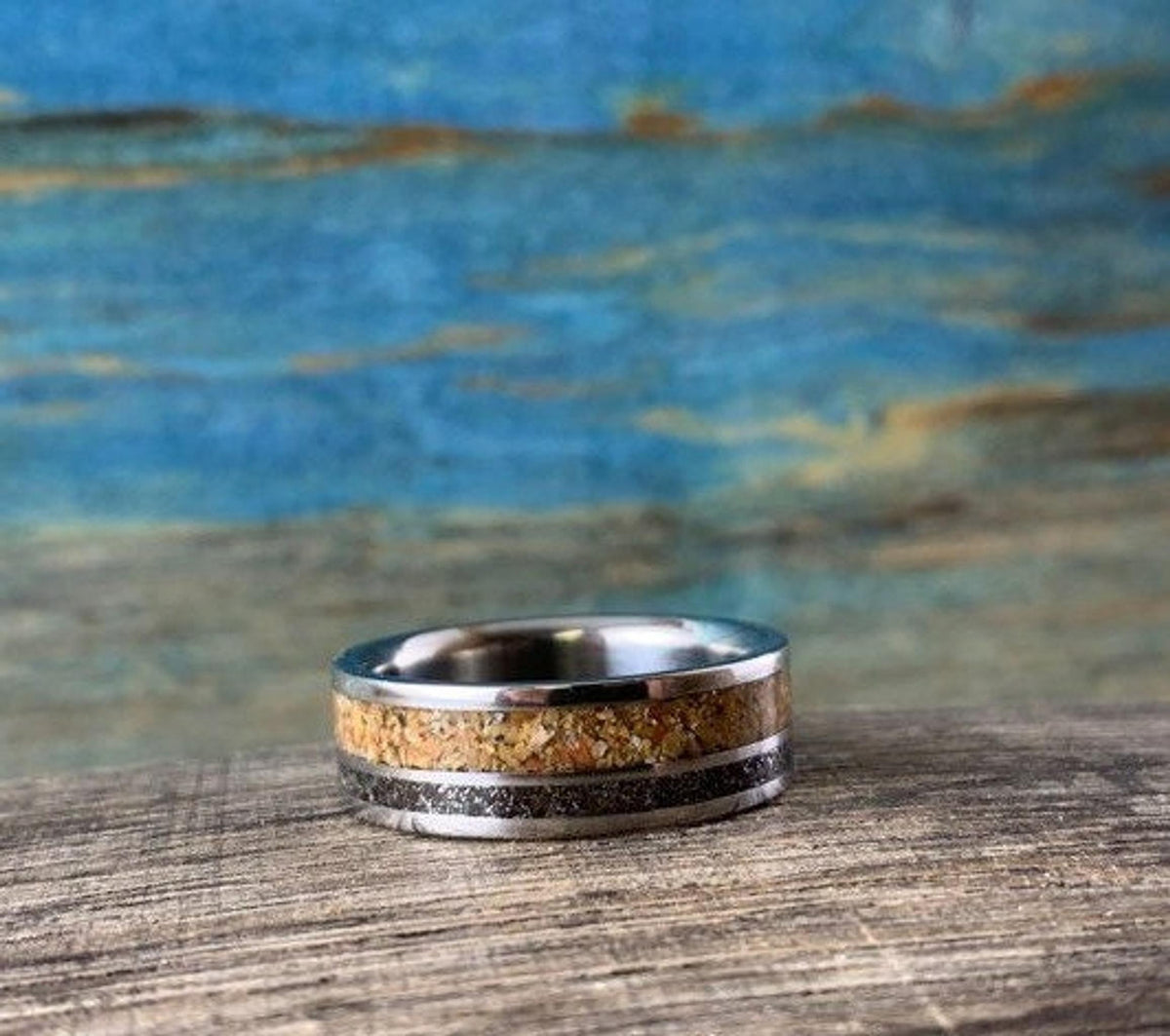 A metal ring with a wood inlay and a dark textured inlay lies flat on a dark wooden surface.