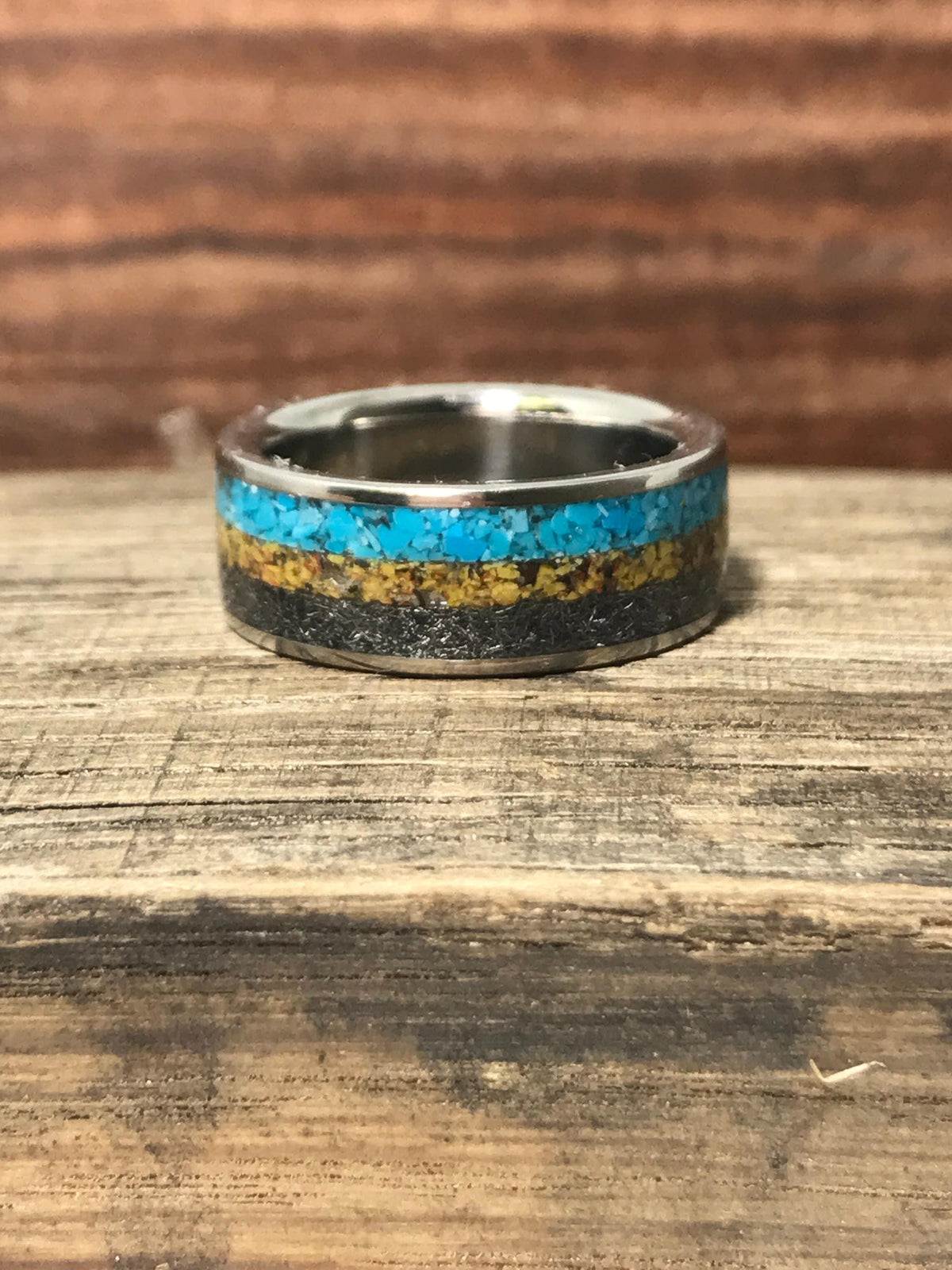 A front view of the inlaid ring resting on a weathered wooden board with a dark brown blurred background.
