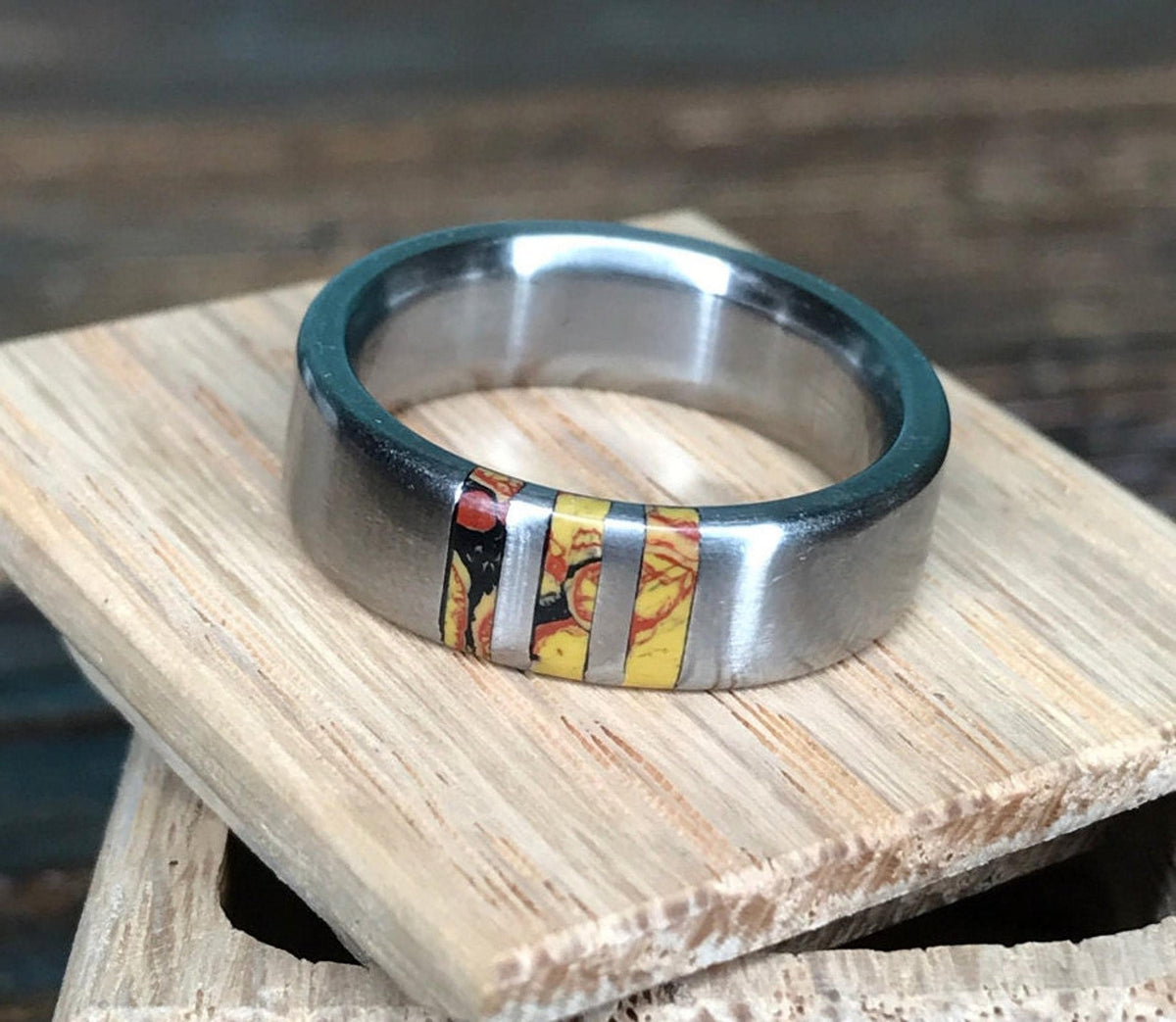 The ring rests horizontally on a small wooden block, showing its patterned inlay and polished interior.