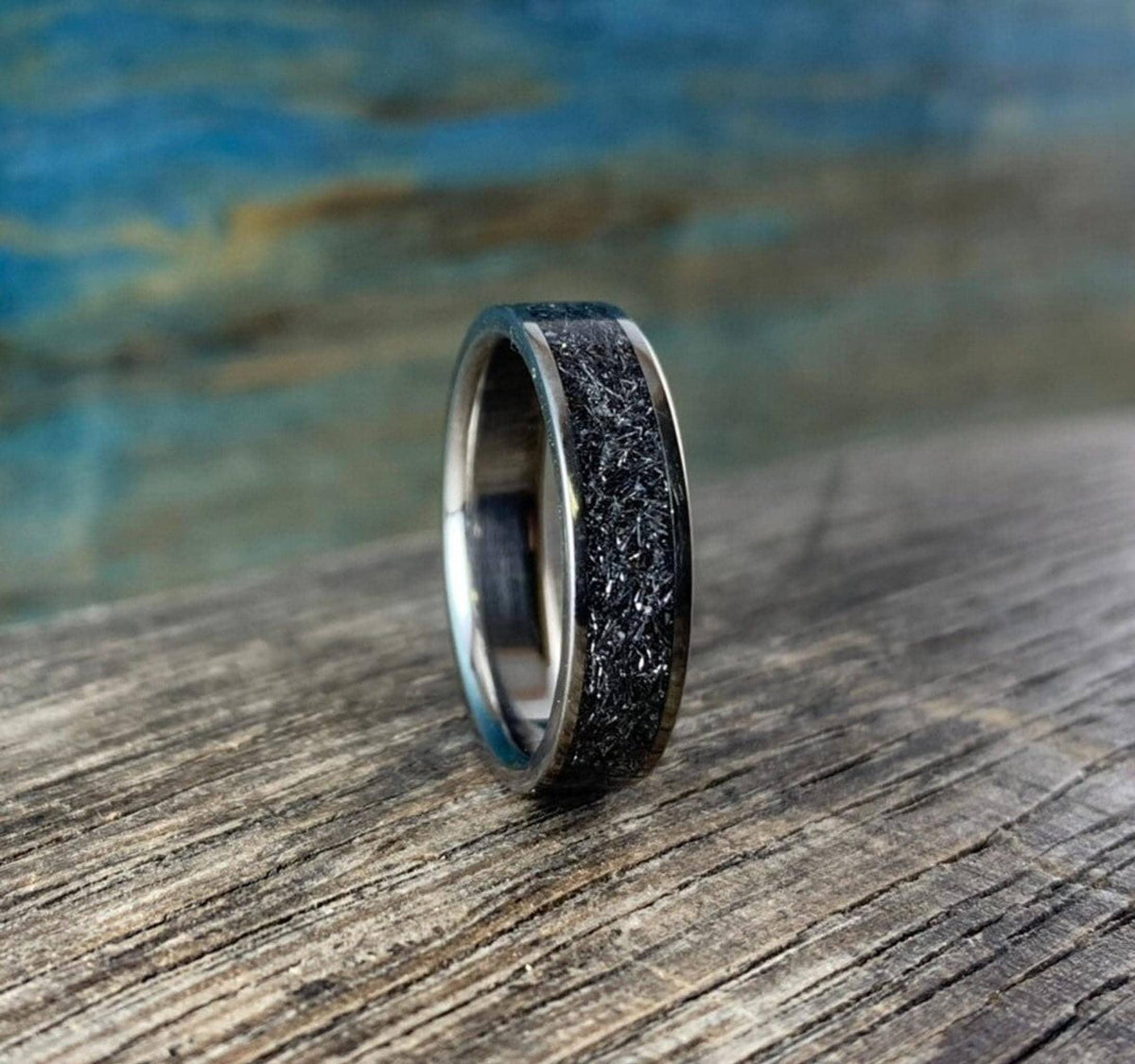 The titanium and meteorite ring is positioned upright and angled slightly on the textured wooden tabletop.