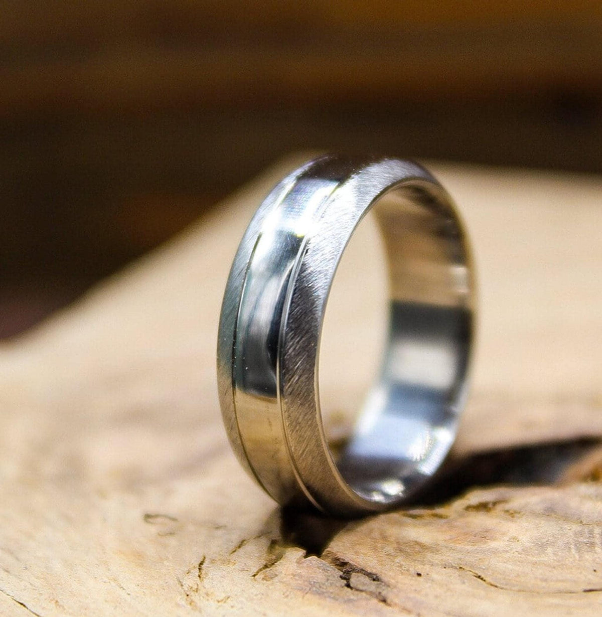 A silver metal ring featuring a brushed finish and a glossy center stripe standing vertically on a wooden surface.