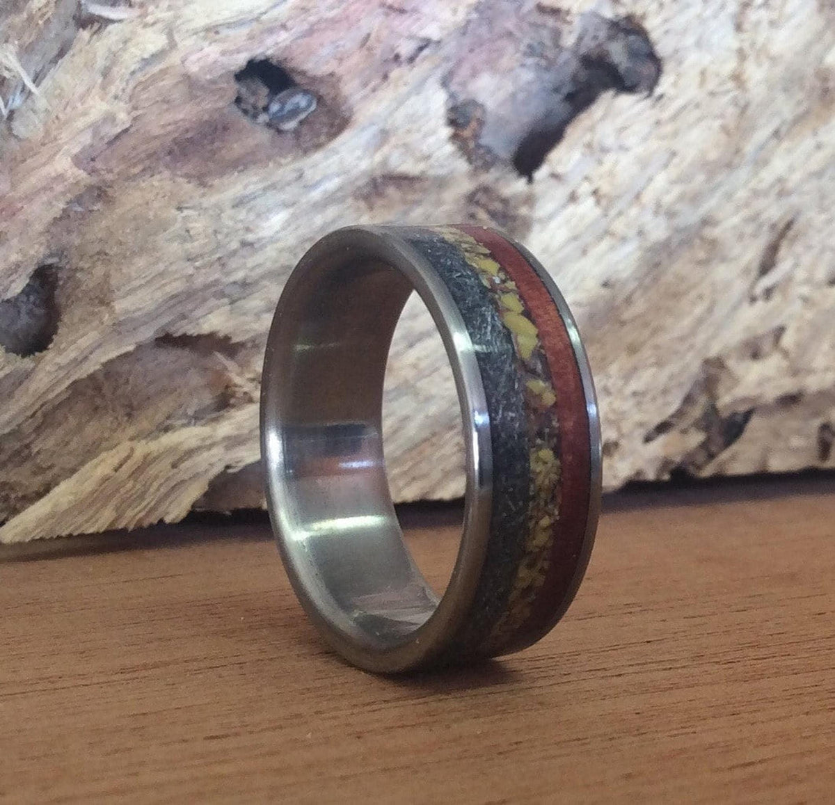 The band ring photographed at a three-quarter angle on a wooden surface with a rough wood slice behind it.