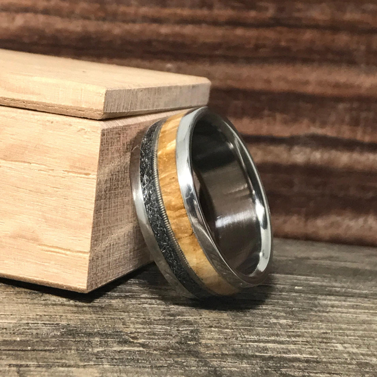 A custom ring angled next to a small wooden ring box on a rustic wooden board.