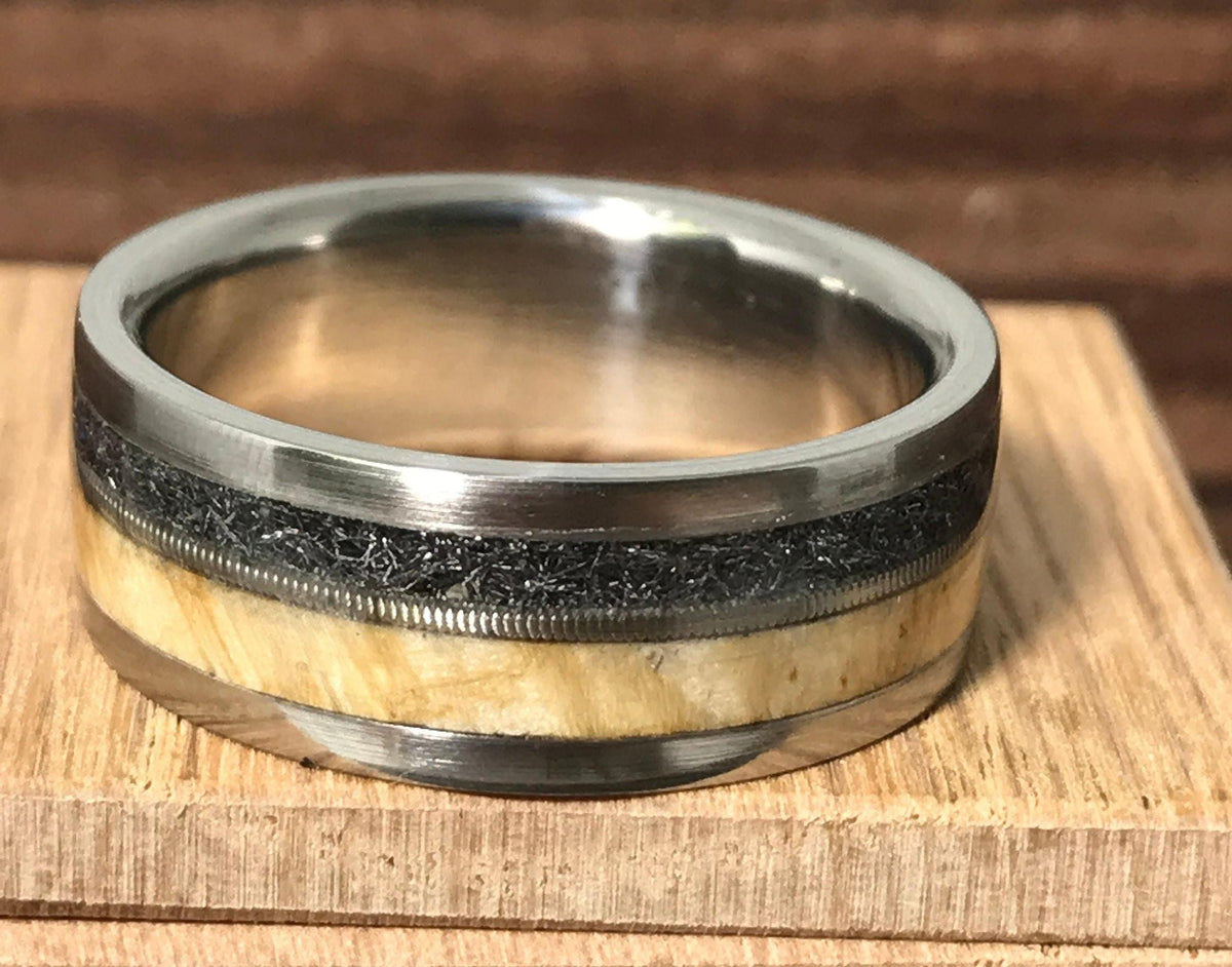 Close-up of a titanium ring with a light wood stripe, a guitar string accent, and a textured meteorite band.