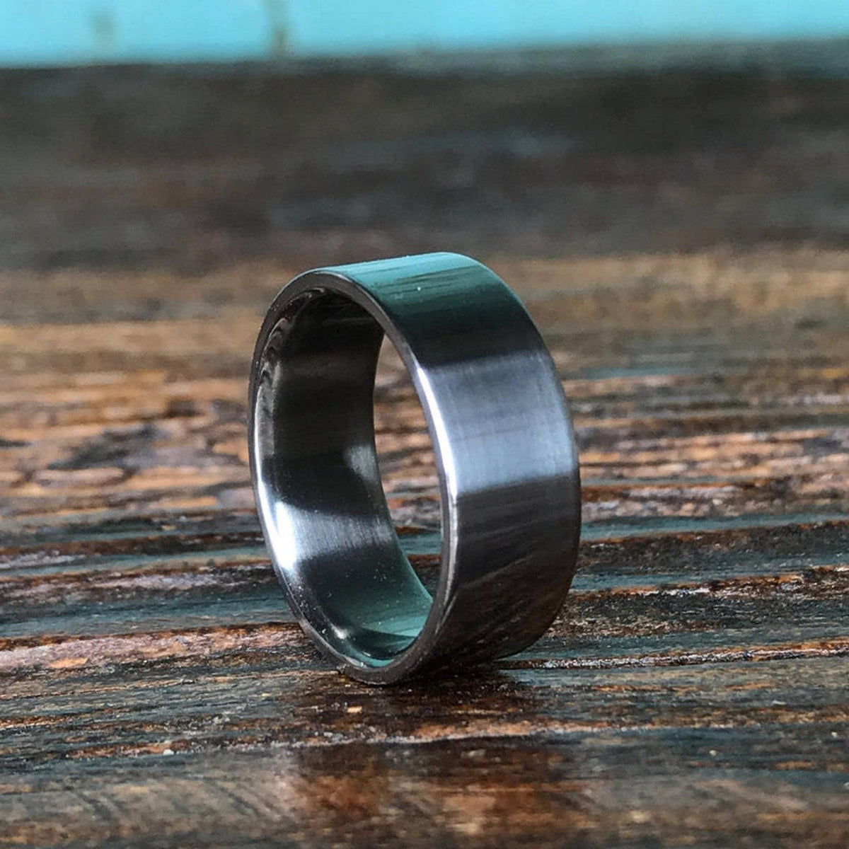 A silver-colored ring sits upright on a weathered wooden tabletop with a blue background.