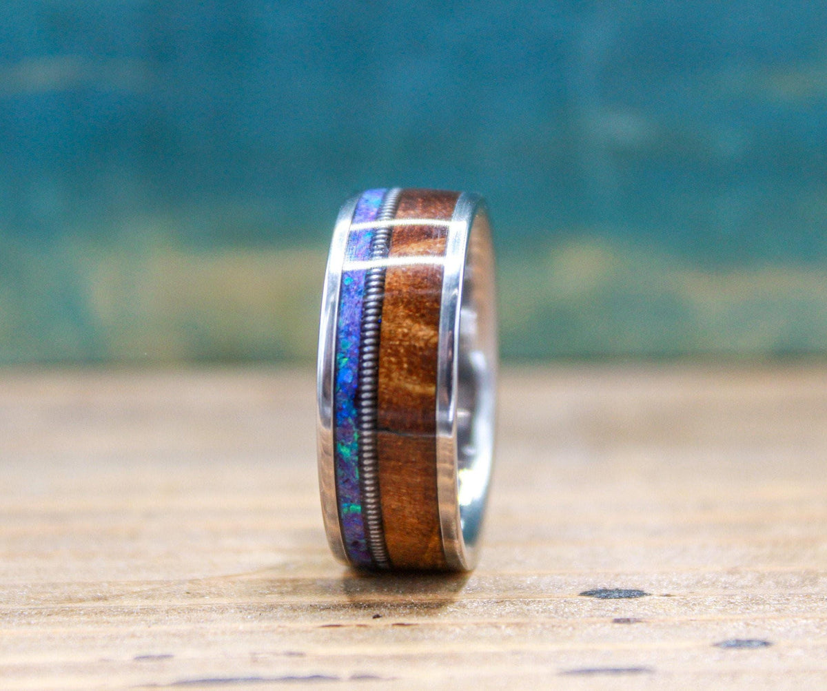 A side view of a titanium ring showing a detailed inlay of wood, metal wire, and purple opal.