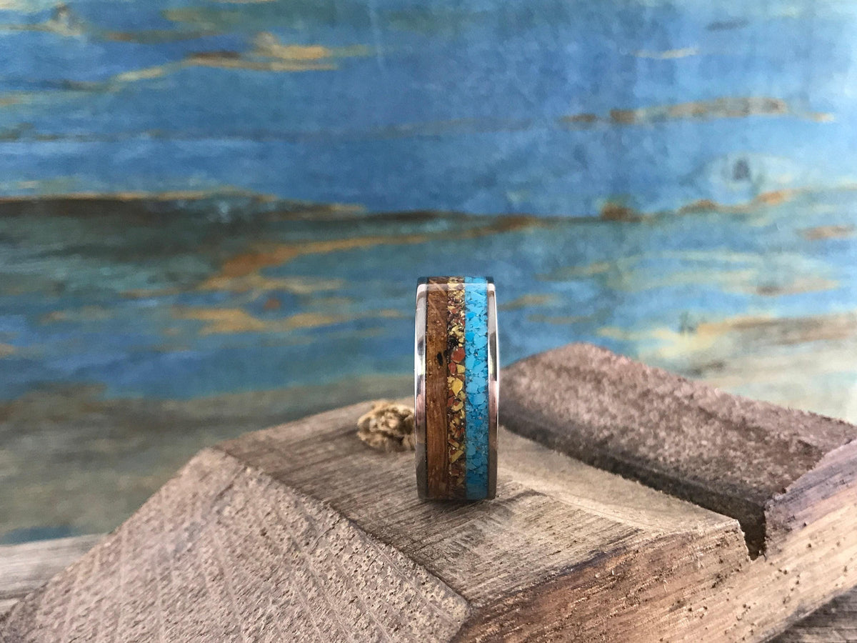 Side view of an artisan ring showing its striped inlay pattern, placed on a dark wooden block.