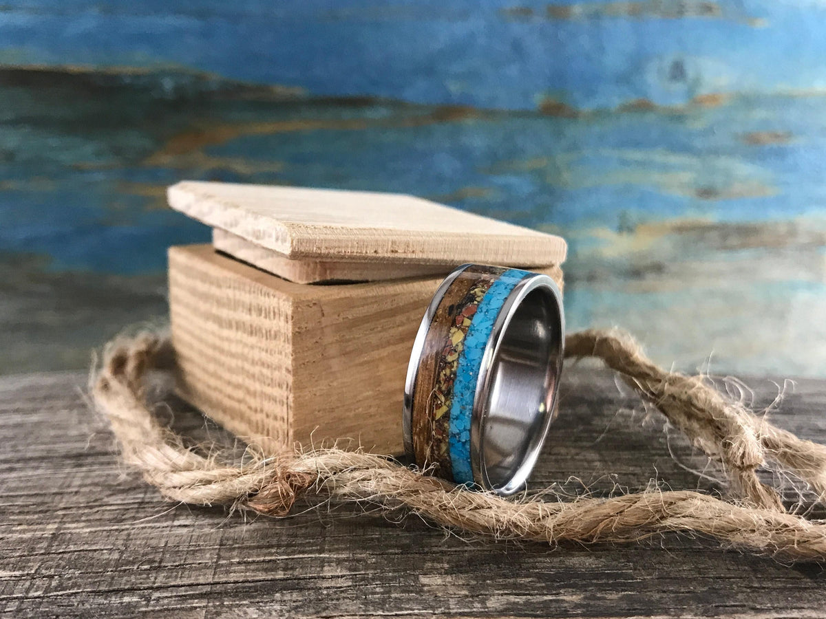 An inlaid ring sits beside a small wooden box and a loop of thick twine on a wooden surface.