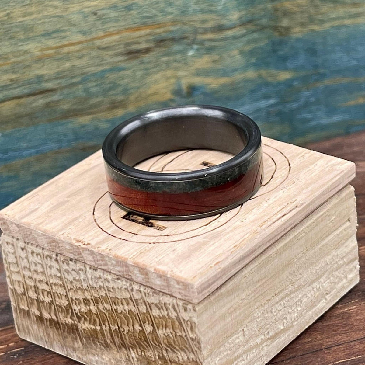 The black ring with red and green inlays rests centered on top of a small wooden storage box.