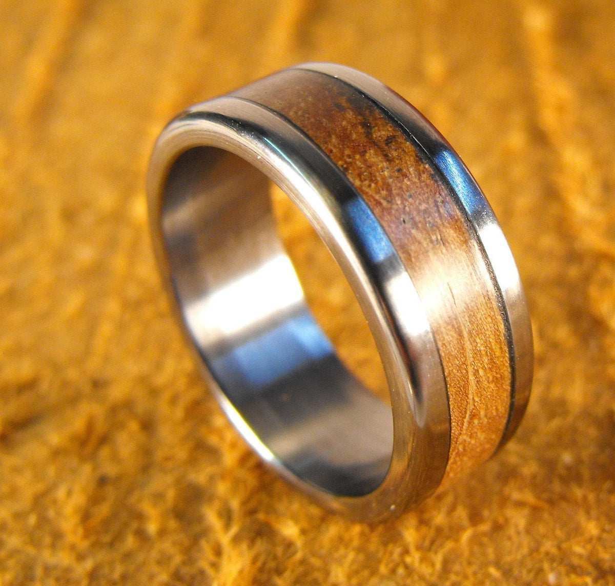 A silver-toned ring with a warm-toned wood inlay, angled on a yellow textured surface.