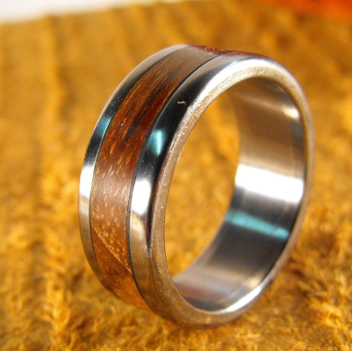 A metal ring with a dark wood inlay, shown upright on a gold fabric background.