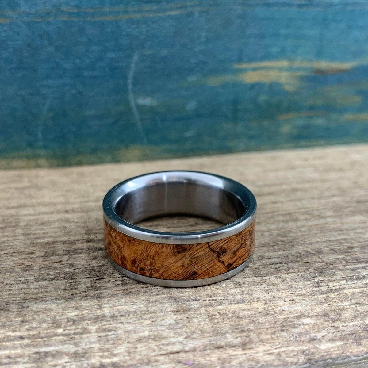 A silver metal and brown wood inlay ring resting flat on a rustic wooden board.
