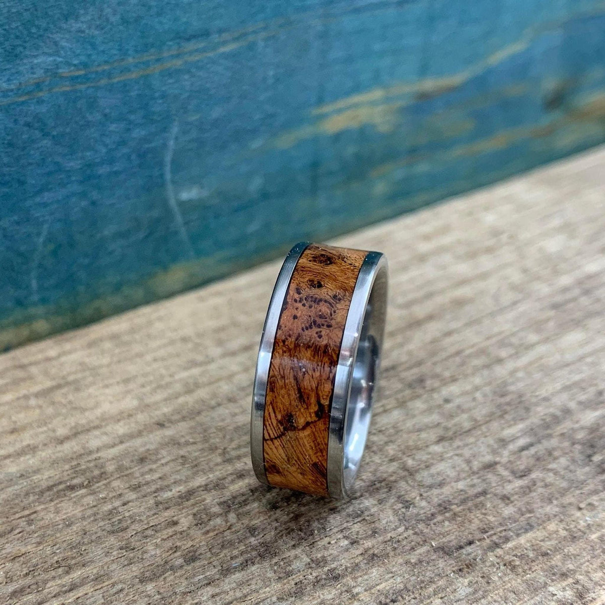 A side profile of a silver metal ring with a detailed brown wood inlay band.
