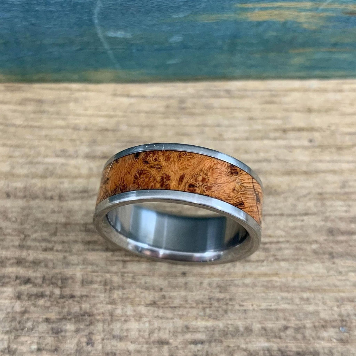 A close-up view of the silver and brown wood ring resting on weathered wood.