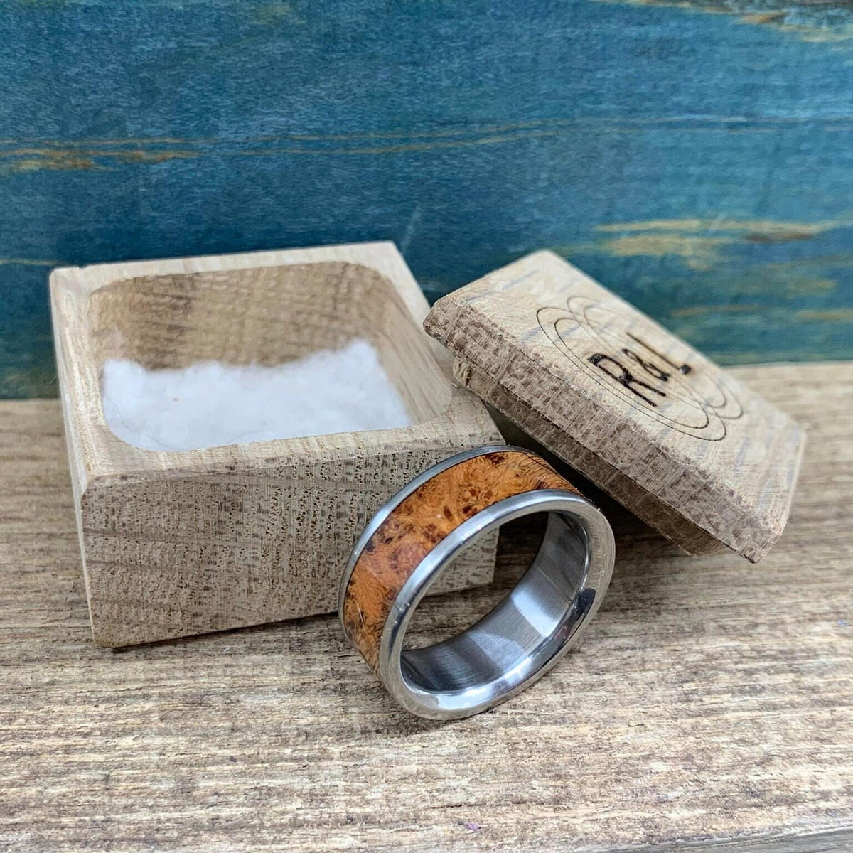 The silver and wood ring placed next to an open wooden ring box lined with white material.