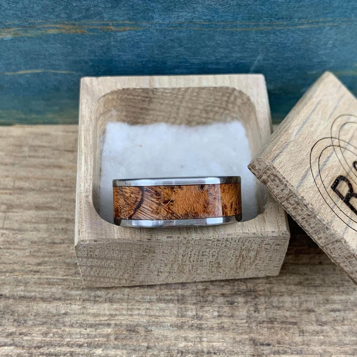 The silver and wood ring resting inside an open wooden box with white padding.