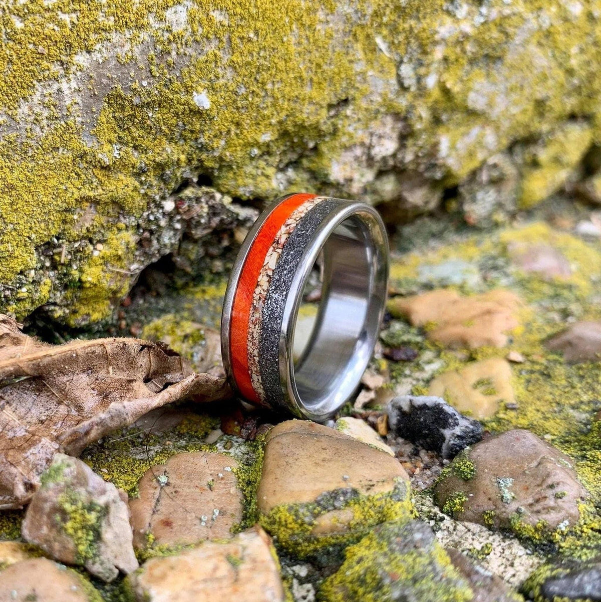 A close-up shot of the inlaid ring angled on mossy rock and gravel.