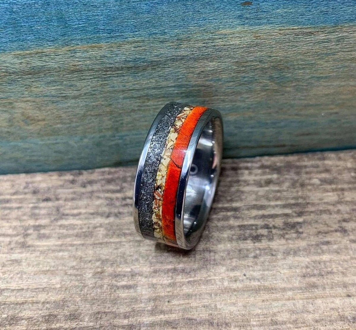 A flat perspective of the multi-inlay ring resting on wood, clearly displaying the red, speckled, and metallic segments.