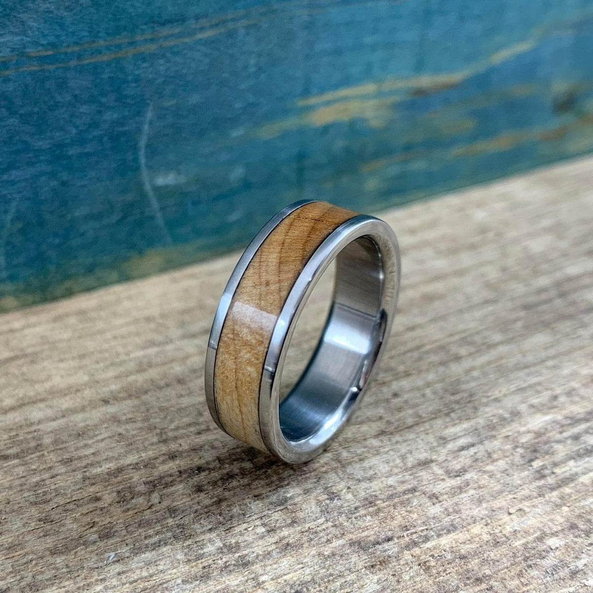 A metal ring featuring a wood inlay stands upright on a rustic wooden surface.