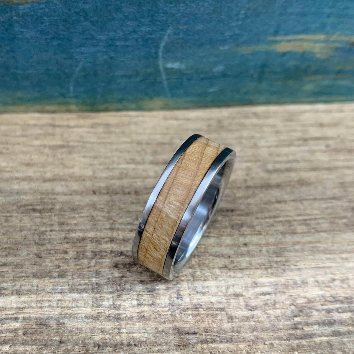 A ring with a light-colored wood band and metal edges is angled on a wooden table.