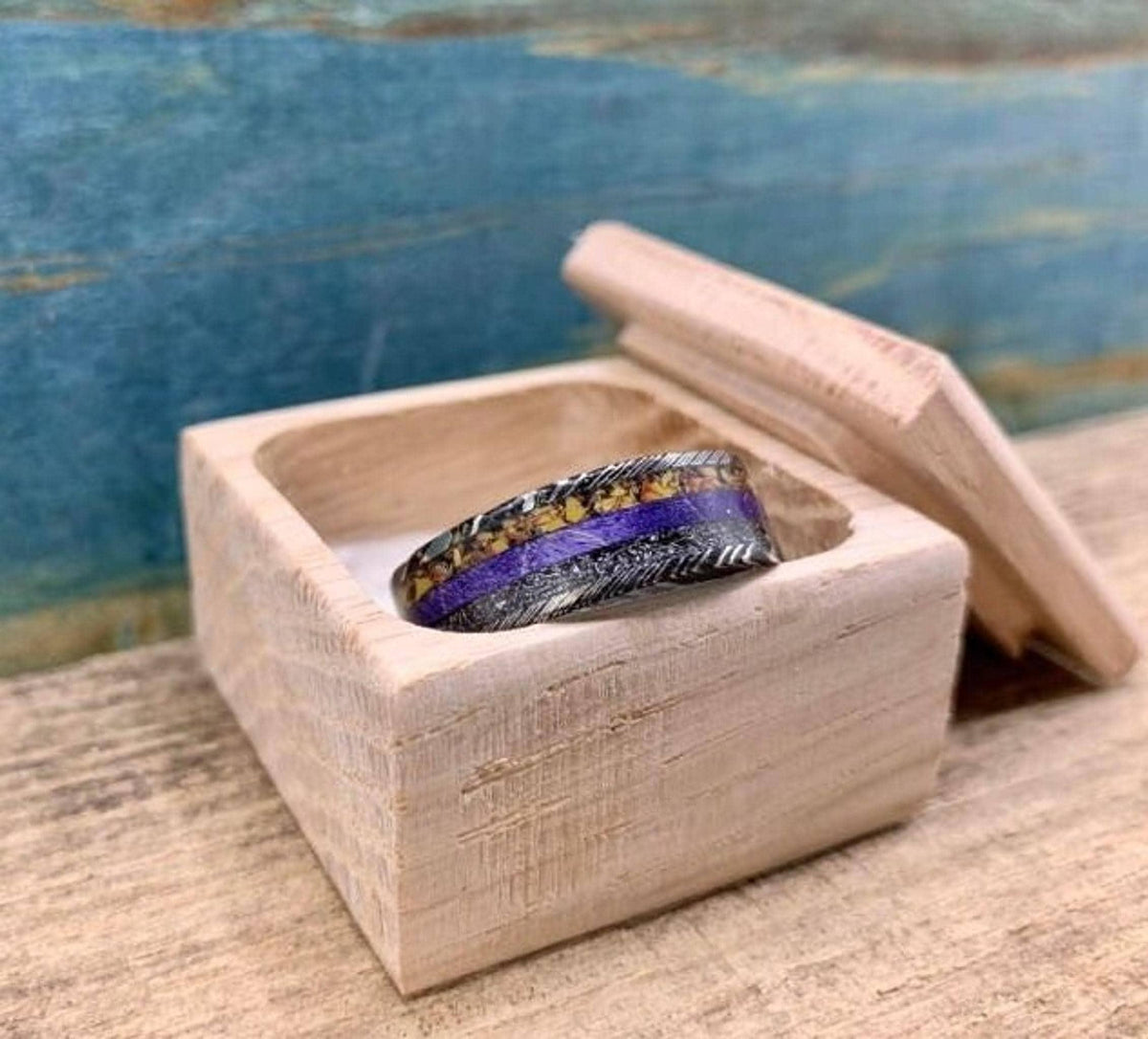 The ring sitting inside a small wooden box with its open lid leaning behind it.