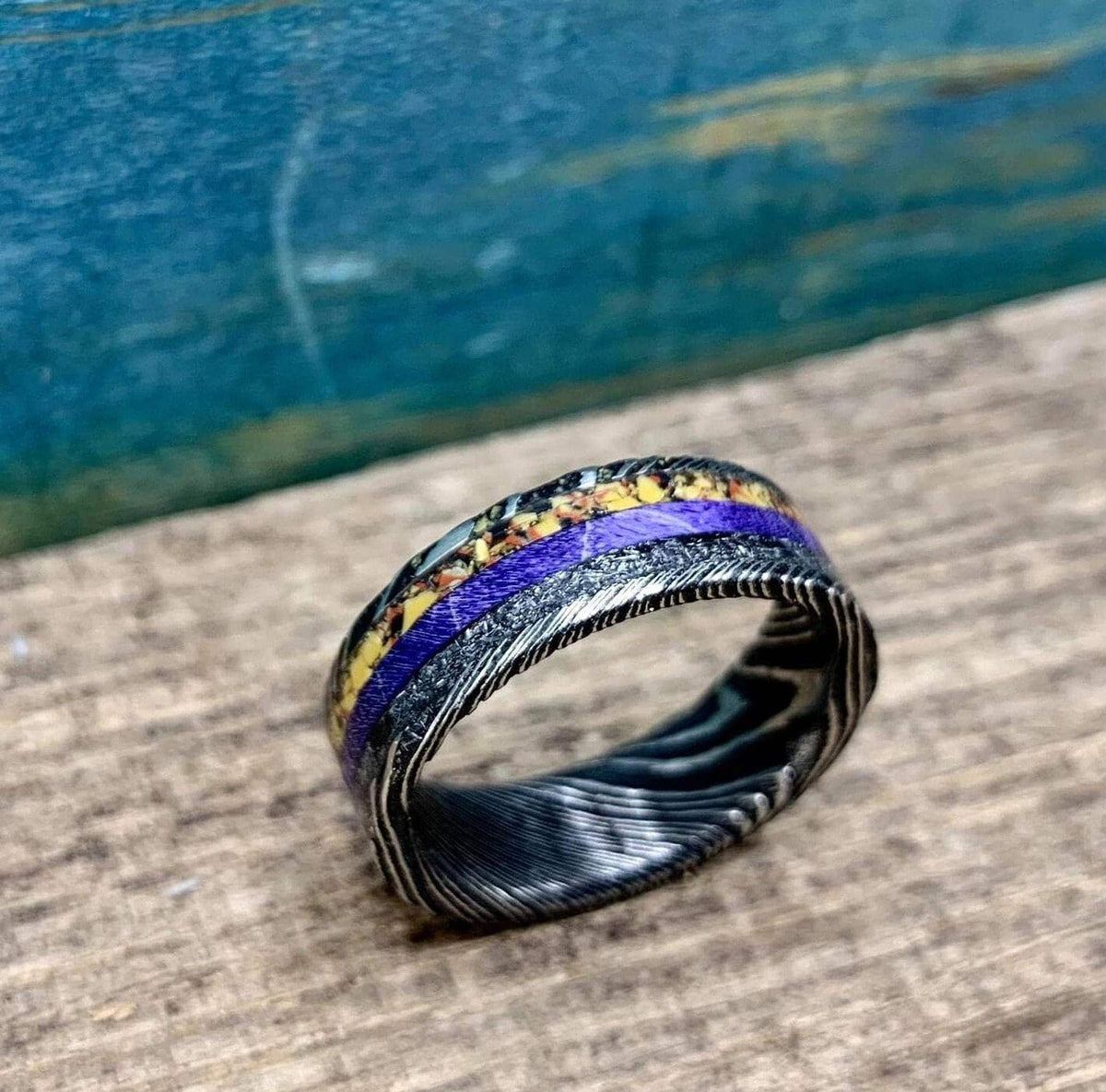 Close-up shot of the ring focusing on the textured Damascus steel edges and colorful inlays.