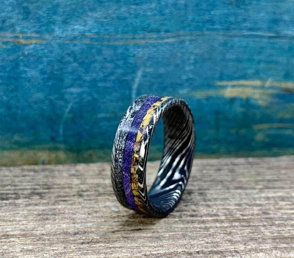 An angled view of the multi-material ring showing the swirling Damascus pattern and inlay details.