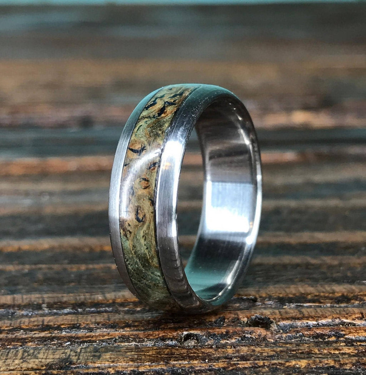 A close-up view of the titanium ring showcasing the organic grain pattern of the black ash burl inlay.