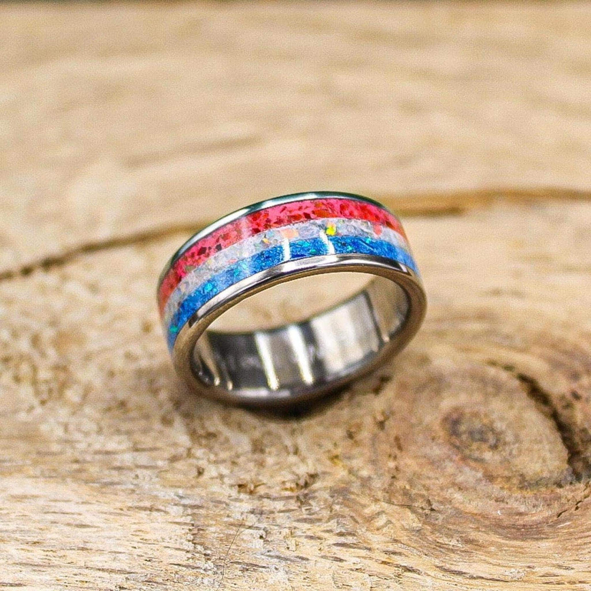 The ring positioned at a three-quarter perspective on the wooden surface, showing the continuous band and sparkling multi-colored inlay.