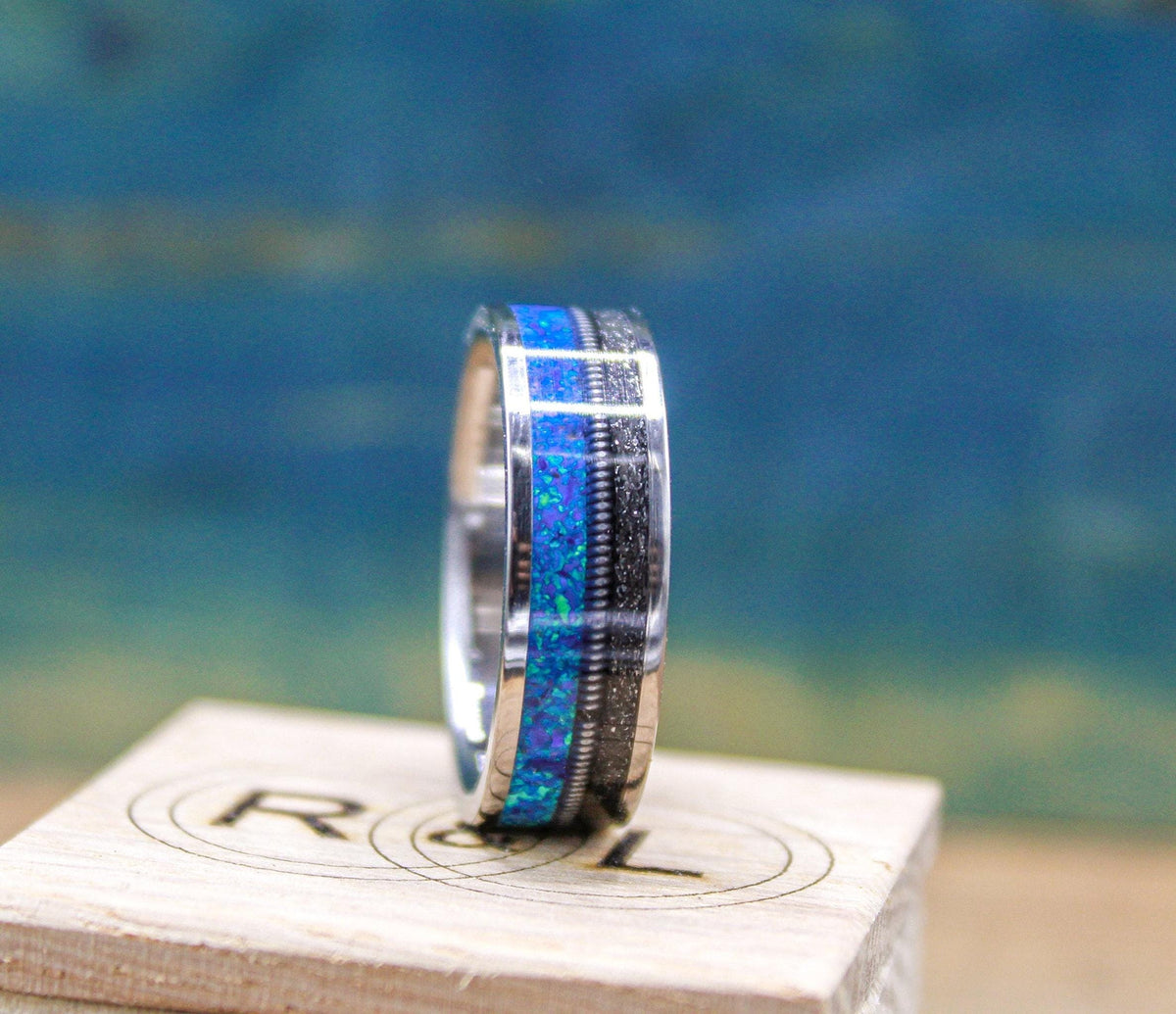 The ring rests on top of a branded wooden box, angled to emphasize the shimmering blue opal inlay.