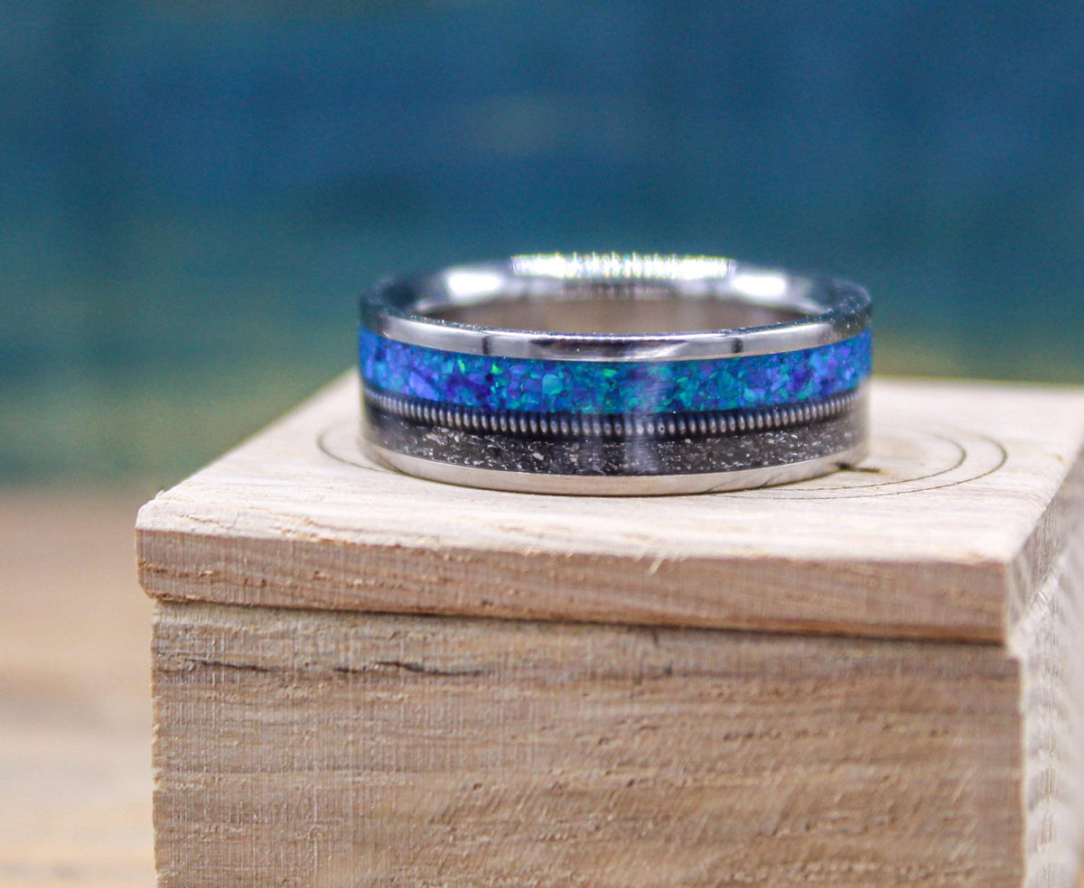 The titanium ring sits upright on a small wooden box, showcasing the contrasting meteorite and blue opal textures.