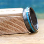 A dark ring with a bright turquoise inlay resting at an angle on a small wooden block.
