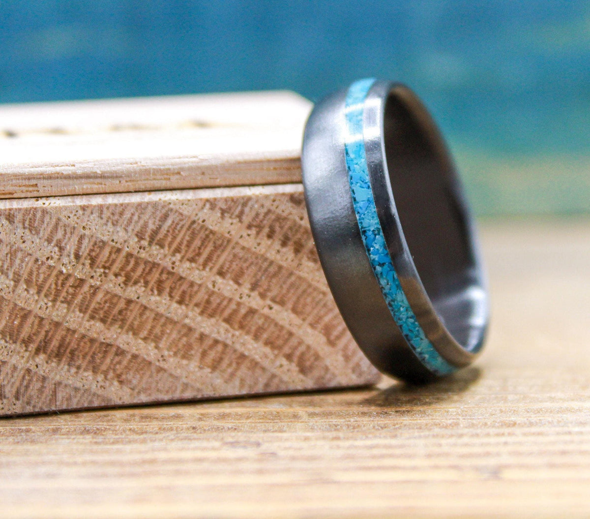A dark ring with a bright turquoise inlay resting at an angle on a small wooden block.