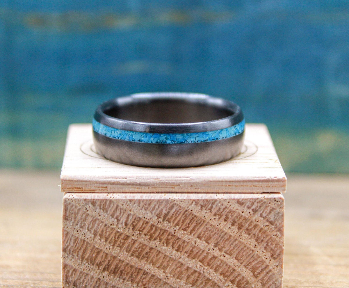 A dark wedding band with a turquoise stripe is centered horizontally on a wooden box.