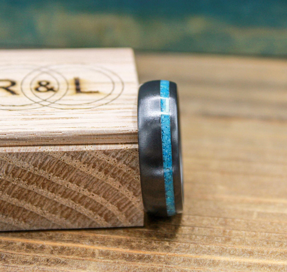 A side profile of a dark metal ring featuring a continuous turquoise inlay line.